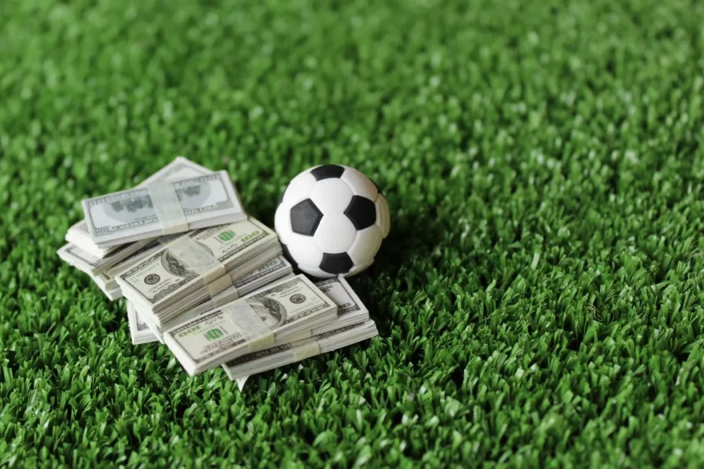 Foto von einem Fußball auf dem Rasen mit einigen Bündeln von Dollar-Scheinen daneben