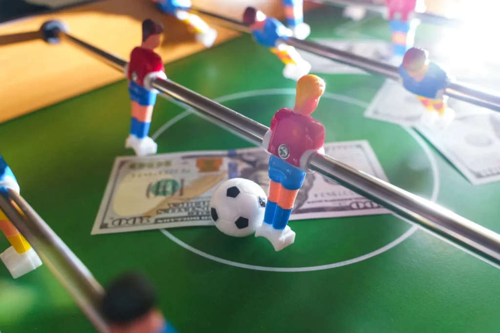 Ausschnitt von einem Tischkicker-Tisch mit Dollar-Scheinen auf der Spielfläche
