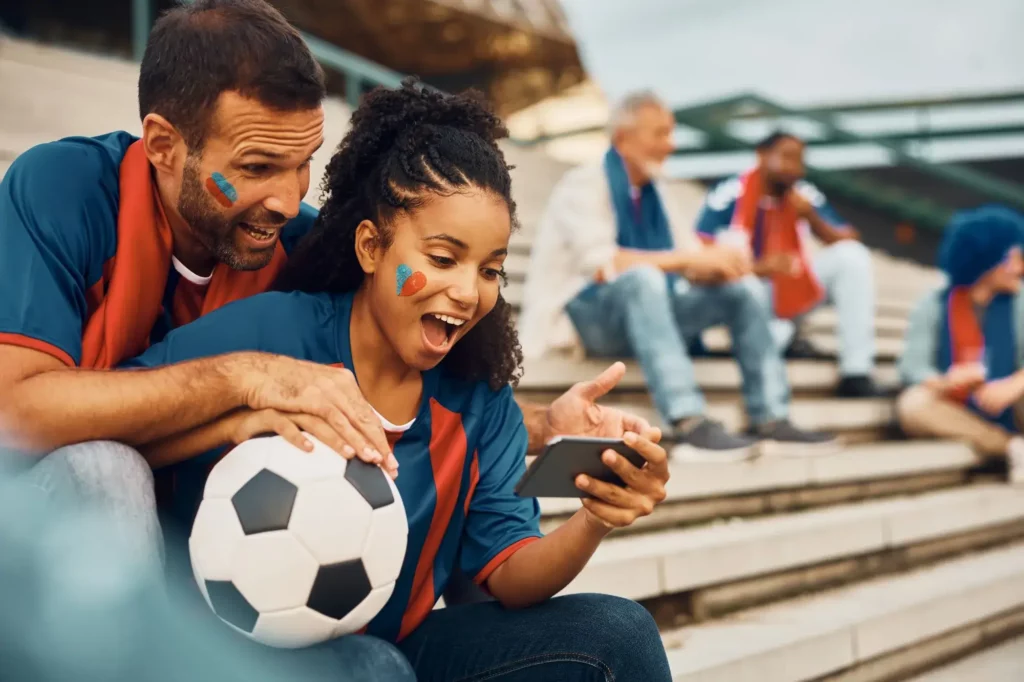 Bunt bemalte und verkleidete Fans schauen Fußball auf dem Smartphone