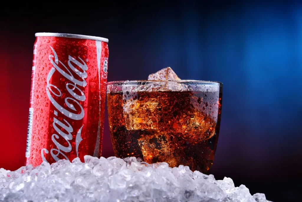 Dose Coca-Cola und ein gefülltes Glas mit Eiswürfeln stehen auf kleinen Eiskugeln