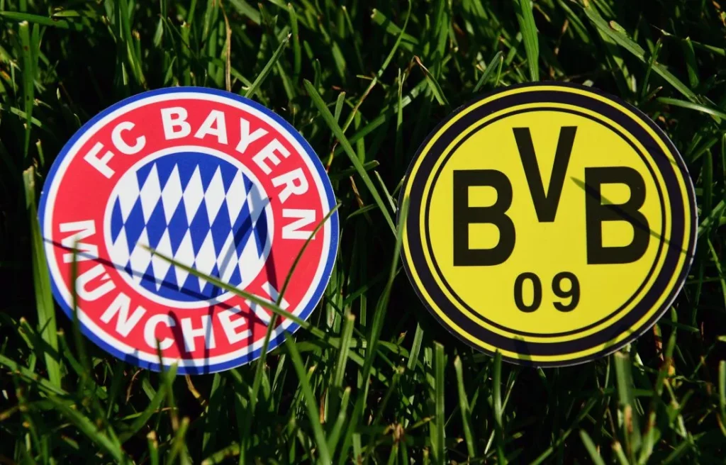 Logos vom FC Bayern München und Borussia Dortmund liegen im Rasen