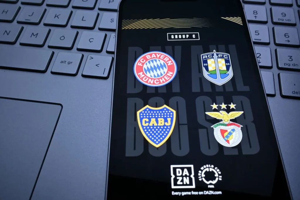 Smartphone auf einer Laptop-Tastatur mit u. a. den Logos von Bayern München und Auckland City auf dem Bildschirm