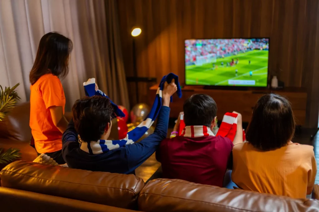 Vier Fußballfans sitzen vor dem Fernseher und schauen sich die Klub WM TV Übertragung an