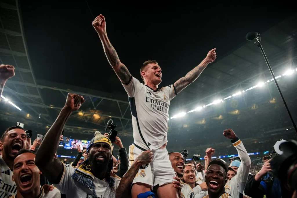 Toni Kroos reißt die Arme hoch und jubelt auf einer Bande vor Menschenmassen